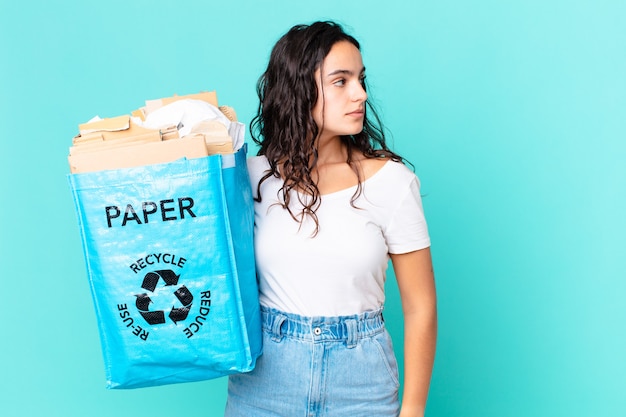 Jolie femme hispanique sur la vue de profil pensant, imaginant ou rêvant et tenant un sac en papier recyclé