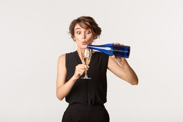 Jolie Femme Ivre Versant Du Champagne Dans Son Verre, Debout Sur Blanc.