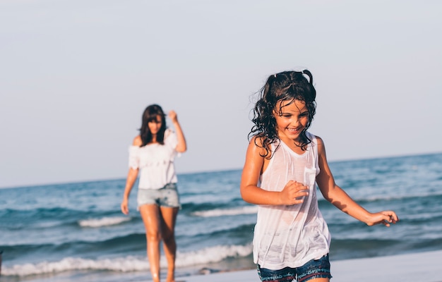 Jolie femme avec un jean bleu court et sa fille jouant dans l'eau de la plage