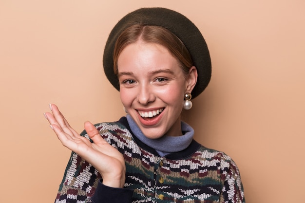 jolie femme joyeuse en boucles d'oreilles posant et souriant à l'avant isolée sur un mur beige