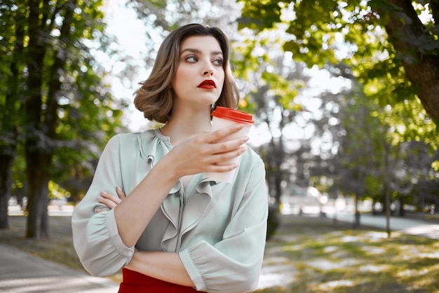 Jolie femme en jupe rouge une tasse de café dans le parc à pied loisirs