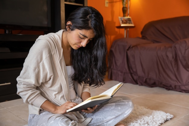 Jolie femme lisant un ordinateur portable à la maison assis sur un tapis à la maison