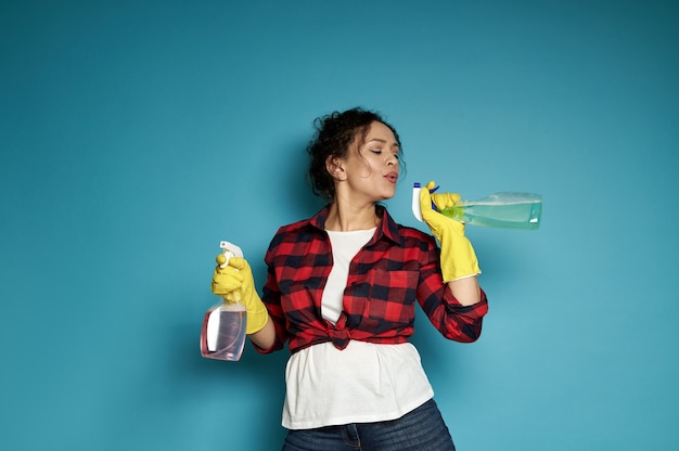 Jolie femme ludique, une femme au foyer, tient un spray nettoyant dans ses mains comme un pistolet et souffle la poudre à canon comme après un tir