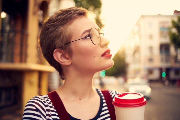 Jolie femme avec des lunettes aux cheveux courts à l'extérieur une tasse de boisson