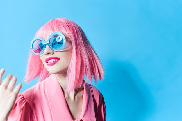 Jolie femme à lunettes bleues porte une perruque rose fond isolé