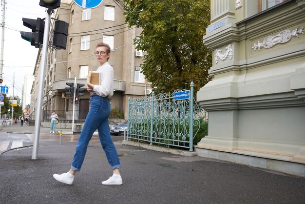 Jolie femme avec des lunettes se promenant dans la ville avec un livre d'éducation