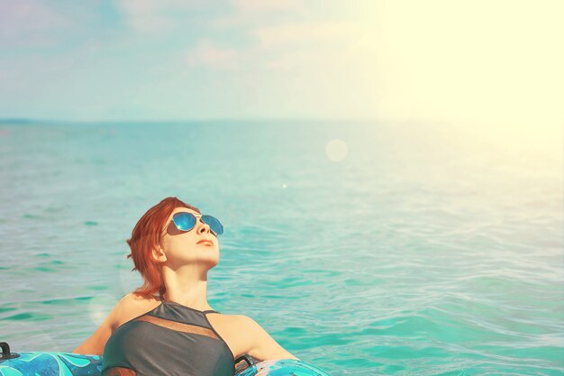 Jolie femme à lunettes de soleil se détendre sur un anneau gonflable dans l&#39;océan