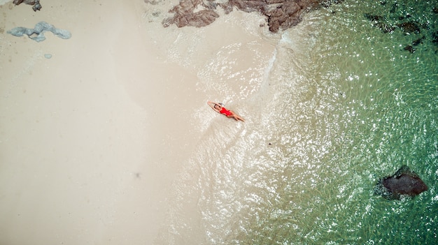 Jolie femme en maillot de bain bikini rouge aime l'eau de mer, le sable brun. Vue à vol d'oiseau prise par un drone. Photo aérienne