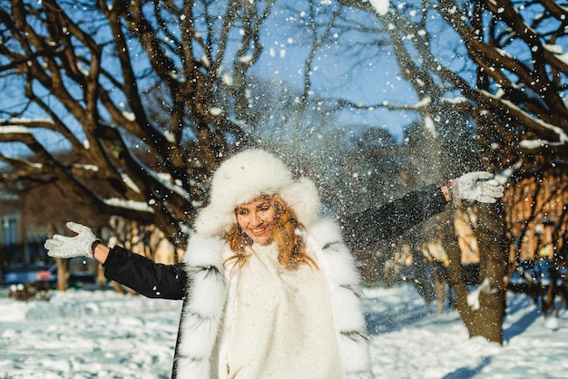 Jolie femme en manteau d'hiver s'amusant avec la neige en plein air