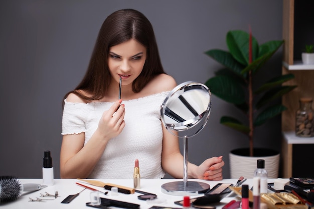 Jolie femme maquillant à la maison devant le miroir.