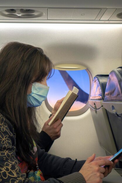 Photo une jolie femme avec un masque dans le siège de l'avion regardant un téléphone intelligent