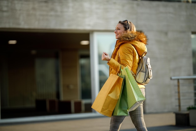 Une jolie femme mature souriante marchant à l'extérieur dans la rue tout en tenant des sacs à provisions.