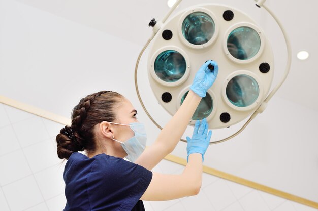 Photo jolie femme médecin dans un masque stérile et des gants en caoutchouc allume une lampe chirurgicale dans un ope moderne