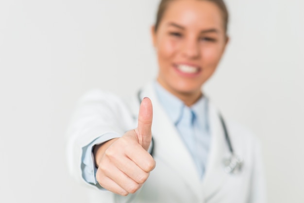 Jolie femme médecin avec un geste positif par le mur blanc