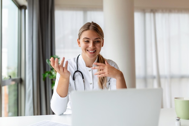 Jolie femme médecin parlant tout en expliquant un traitement médical au patient par le biais d'un appel vidéo avec un ordinateur portable lors de la consultation