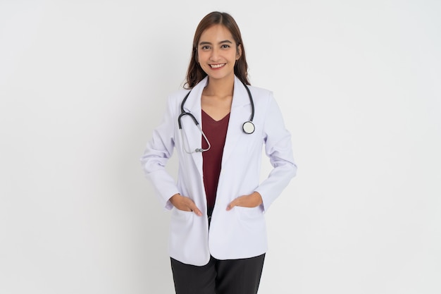 Jolie femme médecin portant un uniforme de costume blanc avec des dents souriantes de bonne humeur avec les mains dans la poche