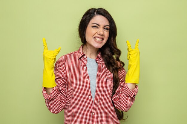 Jolie femme de ménage caucasien excitée avec des gants en caoutchouc faisant des signes de cornes