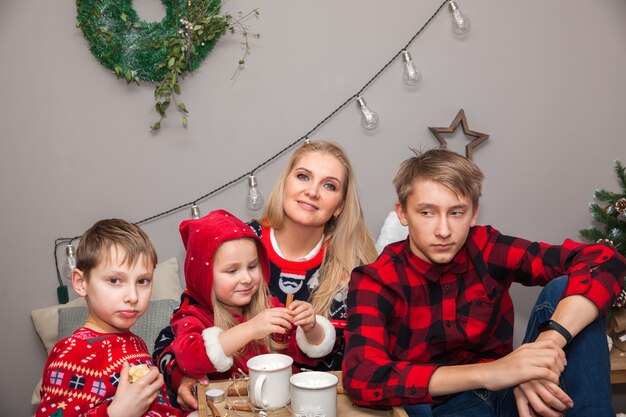 Jolie femme mère avec enfants fille fille et garçons fils assis sur un lit dans une chambre décorée de Noël, look familial, concept du Nouvel An