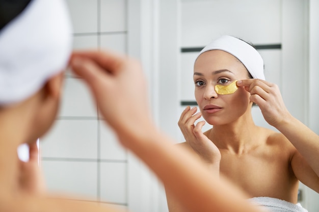 Jolie femme met des patchs sous les yeux dans la salle de bain. Beauté de la peau des yeux