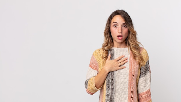 Jolie femme mince se sentant choquée et surprise souriante prenant la main à cœur heureuse d'être celle ou montrant de la gratitude