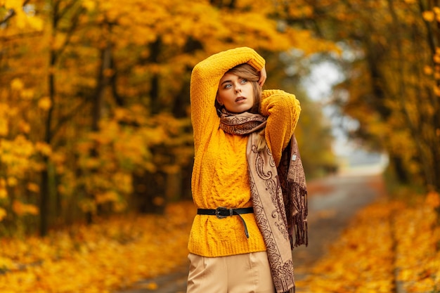 Jolie femme modèle caucasien de mode en pull jaune tricoté vintage et écharpe pose dans un parc d'automne incroyable avec des feuilles jaunes