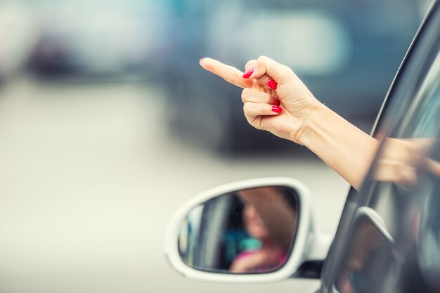 Jolie femme montre un geste obscène d'une voiture.