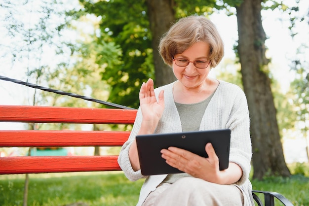 Jolie femme mûre assise sur un banc tenant et utilisant une tablette numérique dans le parc le jour d'été