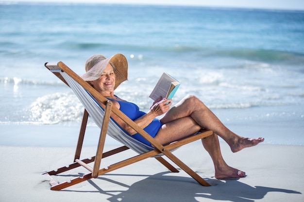 Jolie femme mûre lisant un livre allongé sur une chaise longue