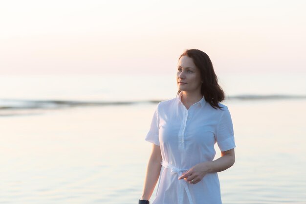 Jolie femme mûre se tient sur la plage et regarde pensivement au loin en mer