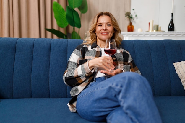 Jolie Femme Mûre Avec Un Verre De Vin Rouge Assis Sur Un Canapé Dans Le Salon