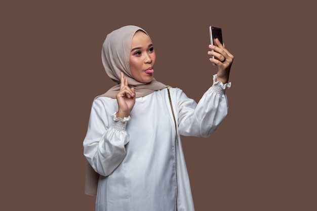 Jolie femme musulmane en hijab prend un selfie à l'aide d'un téléphone intelligent