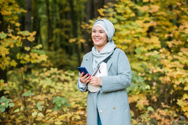 Jolie femme musulmane utilisant un téléphone portable en plein air. Femme arabe portant le hijab à l'aide d'un smartphone. Fille islamique envoyant un message téléphonique dans le parc de la ville. Espace de copie