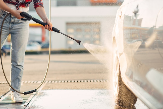 Jolie femme nettoie les roues de la voiture avec un pistolet à eau