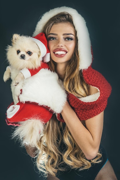 Jolie femme de Noël heureux dans des gants de fourrure blanche avec chien - isolé sur fond noir. Célébration de Noël, nouvel an et vacances. Jolie fille et chien sont vêtus d'un bonnet de Noel rouge. Année du chien.