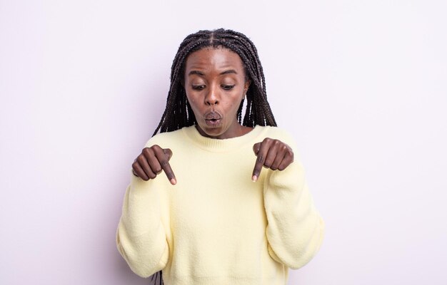 Jolie femme noire avec la bouche ouverte pointant vers le bas avec les deux mains, l'air choquée, étonnée et surprise