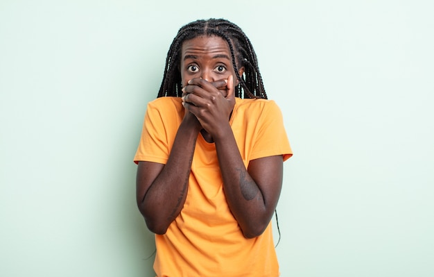 Jolie femme noire couvrant la bouche avec les mains avec une expression choquée et surprise, gardant un secret ou disant oups