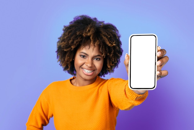 Jolie femme noire montrant un téléphone portable avec écran vide
