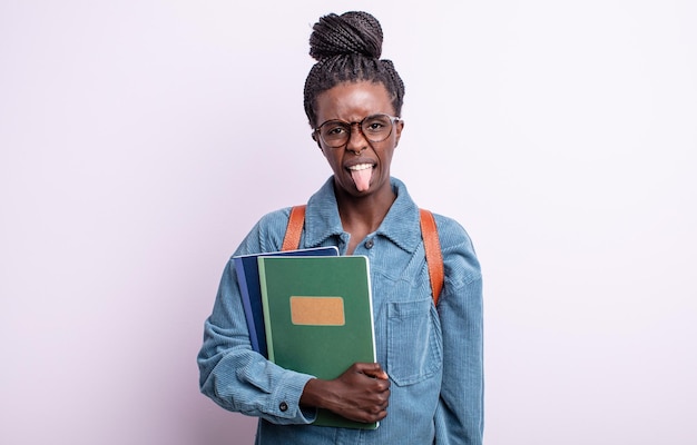 Jolie femme noire se sentant dégoûtée et irritée et tirant la langue. étudiant avec le concept de livres