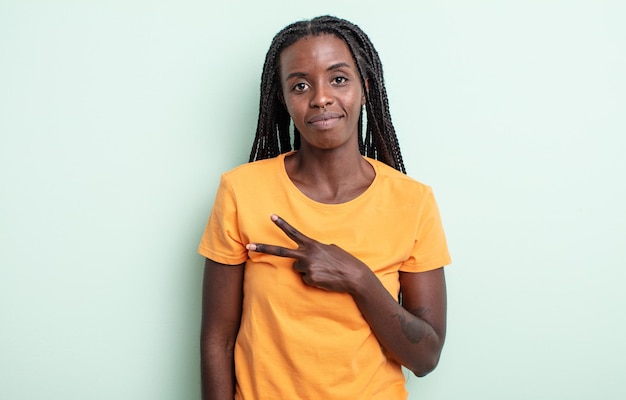 Jolie femme noire se sentant heureuse, positive et réussie, avec la main en forme de v sur la poitrine, montrant la victoire ou la paix