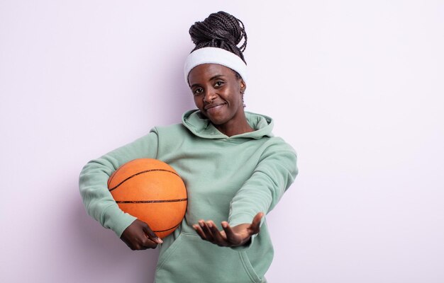 Jolie femme noire souriant joyeusement avec amicale et offrant et montrant un concept. concept de basket-ball