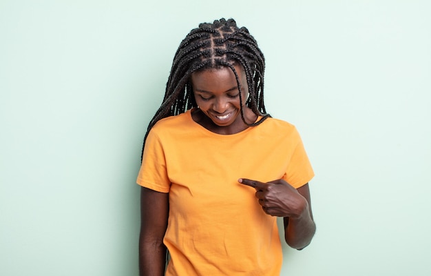 Jolie femme noire souriant joyeusement et avec désinvolture, regardant vers le bas et pointant vers la poitrine