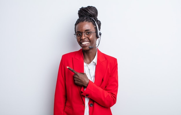 Jolie femme noire souriant joyeusement, se sentant heureuse et pointant sur le côté. concept de télémarketing