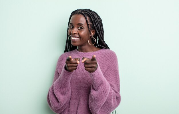 Jolie femme noire souriante avec une attitude positive, réussie et heureuse pointant vers la caméra, faisant un signe de pistolet avec les mains