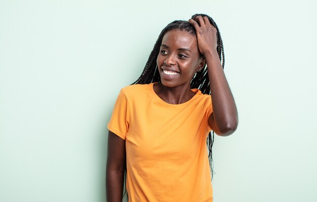 Jolie femme noire souriante joyeusement et avec désinvolture, prenant la main à la tête avec un regard positif, heureux et confiant