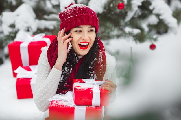 Jolie femme parlant sur un téléphone mobile et tenant des cadeaux de Noël.