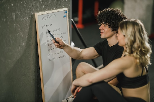 Une jolie femme parle de plan d'exercice avec son entraîneur personnel au gymnase.