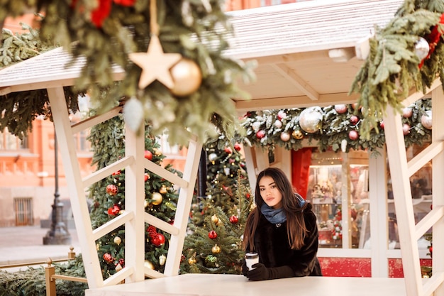 Jolie femme passe du temps à l'extérieur à la foire de noël une tasse de café dans les mains des filles