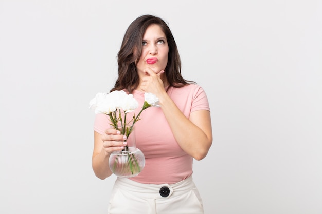 Jolie femme pensant, se sentant dubitative et confuse et tenant un pot de fleurs décoratif