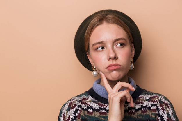 jolie femme pensante en boucles d'oreilles posant et regardant vers le haut isolée sur un mur beige