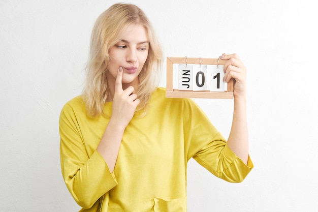 Une jolie femme perplexe en vêtements jaunes avec calendrier pense à se préparer pour un voyage de vacances, il ne reste plus beaucoup de temps avant le premier jour de l'été